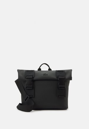 Sac bandoulière noir texturé avec fermeture roulante, deux grandes boucles à l'avant, une poignée supérieure et une bandoulière ajustable.