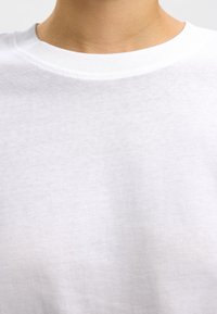Weißes Baumwoll-T-Shirt mit Rundhalsausschnitt und glatter Textur. Nahansicht zeigt minimale Nähte und gleichmäßige Stoffoberfläche.