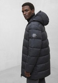 Czarna kurtka puchowa z kapturem, zapinana na zamek z przodu, pikowana, z logo marki na rękawie. Gładka tekstura i standardowy krój.