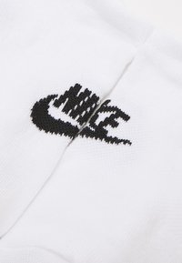 Calcetín de algodón blanco con un logo de Nike negro, con una textura suave y un diseño acanalado en la parte superior. Costura visible en un lado.