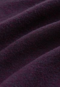 Mély bordó színű, texturált szövet, lágy, kötött felülettel, enyhe árnyalatváltozásokkal, amelyek kiemelik a melegségét és mélységét.