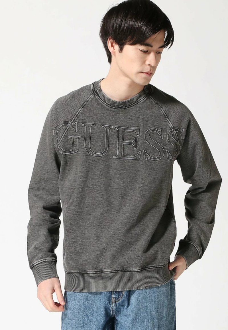 Felpa grigia con polsini e orlo a costine, caratterizzata dal logo "GUESS" in lettere in rilievo. Design con collo a giro e maniche raglan. Tessuto morbido.
