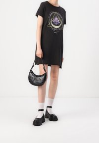 Black t-shirt dress features a lotus graphic, paired with a black studded handbag and chunky black shoes with ankle straps and white socks.