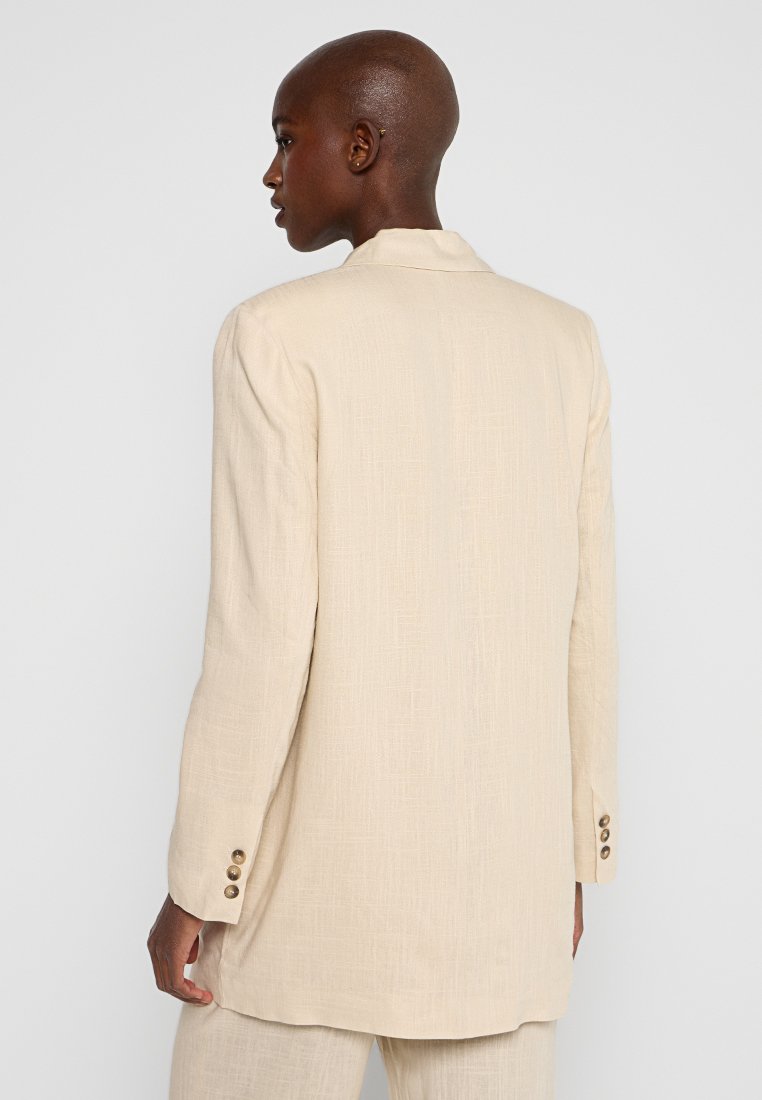 Beige Leinenblazer mit lässigem Schnitt, langen Ärmeln und drei Knopfakzenten an den Manschetten, mit einer dezenten strukturierten Oberfläche.
