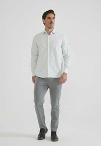 Chemise boutons-pression bleu clair, pantalon texturé gris et chaussures noires. Coupe slim avec un col pointu, taille plate et tissu lisse.