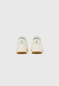 White slip-on sneakers with gum soles shown from the back, featuring green "Slip-Ins" logo on the heel tab.
