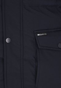 Granatowa, pikowana kurtka o gładkiej fakturze, z klapką kieszeni, zatrzaskami i małym logo na kieszeni.