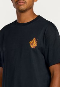 T-shirt en coton noir à manches courtes et col rond, présentant un design graphique coloré sur la partie gauche de la poitrine.