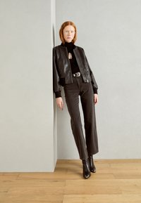 Chaqueta bomber de cuero negro con puños acanalados, combinada con jeans negros de cintura alta y botines negros de punta. Diseño minimalista.