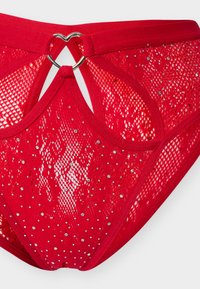 Κόκκινο εσώρουχο από δαντέλα με διακοσμητικά στρας και λεπτομέρεια στην ζώνη με μεταλλικό δαχτυλίδι σε σχήμα καρδιάς.
