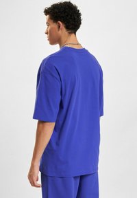 Oversized blauwe katoenen t-shirt met korte mouwen, een ronde hals en een gladde textuur, weergegeven van achteren met zichtbare stikseldetails.