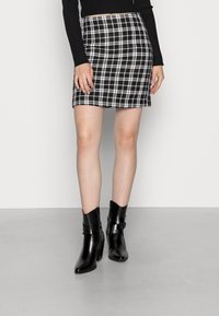 Svartvitt rutigt minikjol med en figurnära design, tillsammans med blanka svarta ankelstövlar med remdetalj och kraftig klack.