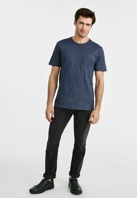 Granatowa koszulka z krótkim rękawem z kieszonką na piersi, wykonana z teksturowanej tkaniny. W zestawie z ciemnymi dżinsami i czarnymi sneakersami.