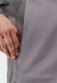 Siva, teksturirana tkanina odjeće s labavim krojem, s bočnim šavom gdje ruka dodiruje tkaninu, naglašavajući meki materijal.