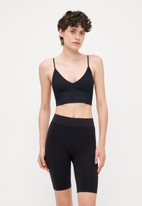 Black sports bra with adjustable thin straps and a deep V-neck, paired with high-waisted black shorts, both made of smooth fabric.
