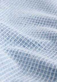 Tissu bleu clair avec un motif gaufré texturé créant une grille de petits carrés en relief.