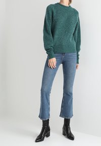 Teal värviga kootud sviiter pikkade varrukatega, talje juures istuv, kantud laienevate siniste teksade ja mustade läikivate nilkkadega saapadega.