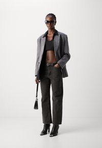 Blazer gris con un top corto negro, jeans negros de cintura alta y botas de tacón negras. Los accesorios incluyen un pequeño bolso negro y gafas de sol.
