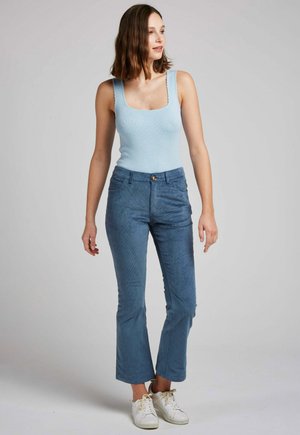 Top en maille côtelée bleu clair associé à un pantalon tapered bleu foncé avec fermeture à bouton et poches avant. Le modèle porte des baskets blanches.