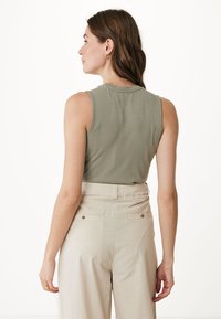 Débardeur côtelé vert olive, sans manches avec un col rond, associé à un pantalon beige taille haute avec des accents de boutons.