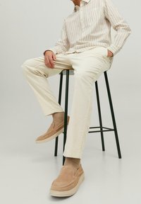 Beige slip-on shoes, cream pants, and a striped shirt. Textured fabric, relaxed fit, and subtle patterns. Lightweight and casual appearance.