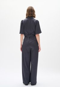 Completo grigio scuro con maniche a sbuffo corte, vita con cintura e design a gambe larghe. Tessuto liscio con una sottile texture e accenti minimali.