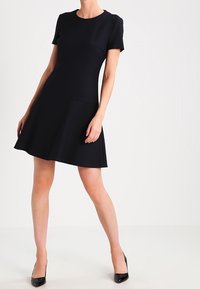 Černé šaty s krátkými rukávy a přiléhavým korzetem, se splývavou sukní. Hladký materiál bez vzorů. V kombinaci s černými vysokými podpatky.