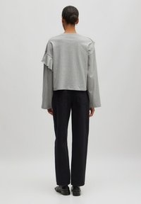 Grauer, gekürzter Pullover mit Rüschendetail an den Schultern, kombiniert mit dunklen, geraden Hosen, von hinten gesehen. Glatte Stofftextur.