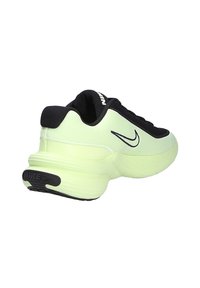 Zapatilla de running Nike en verde claro y negro, vista en ángulo para mostrar el lateral y el talón, con el logo swoosh negro y suela gruesa sobre fondo blanco.