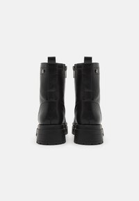 Une paire de bottines noires en cuir avec des semelles épaisses et des tirettes à l'arrière, présentées de l'arrière sur fond blanc.