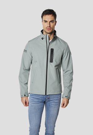 Chaqueta softshell gris claro con cuello alto, bolsillo en el pecho con cremallera negra y bolsillos laterales. Corte entallado con puños ajustables.