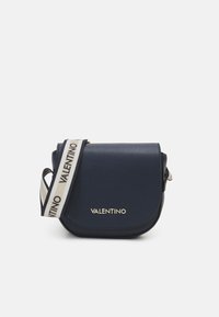 Granatowa skórzana torba na ramię z okrągłą klapką, złotym logo oraz regulowanym paskiem w paski z powtarzającym się wzorem nazwy marki.