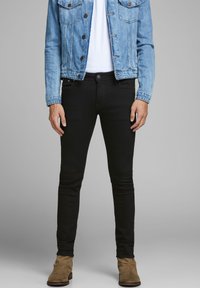 Vaqueros ajustados negros con una textura suave, bolsillos frontales y cierre de botón, combinados con una chaqueta de mezclilla azul clara.