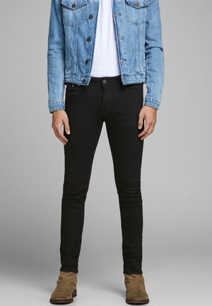 Vaqueros ajustados negros con una textura suave, bolsillos frontales y cierre de botón, combinados con una chaqueta de mezclilla azul clara.