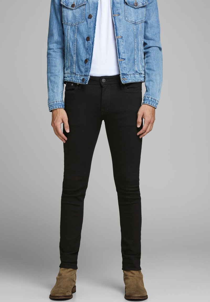 Vaqueros ajustados negros con una textura suave, bolsillos frontales y cierre de botón, combinados con una chaqueta de mezclilla azul clara.