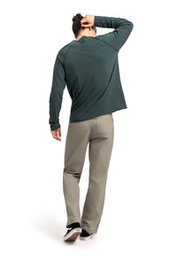 Camicia a maniche lunghe di colore verde scuro con scollo rotondo, maniche inserite e pantaloni grigi chiari. Sneakers nere con dettagli bianchi.