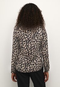 Top a maniche lunghe con stampa leopardo, realizzato in tessuto leggero e morbido di colore beige, con macchie nere e marroni, orlo arrotondato e maniche aderenti.