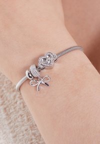 Pulsera de encanto de plata con charms de corazón, cuentas y lazo; diseño elegante con textura suave y acentos brillantes.