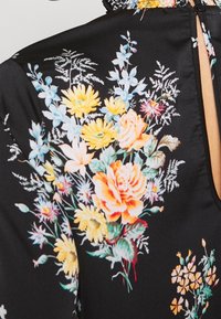 Tissu noir avec un imprimé floral featuring des marguerites jaunes, des roses roses et des fleurs bleues, mettant en avant une texture lisse et un design à dos ouvert.