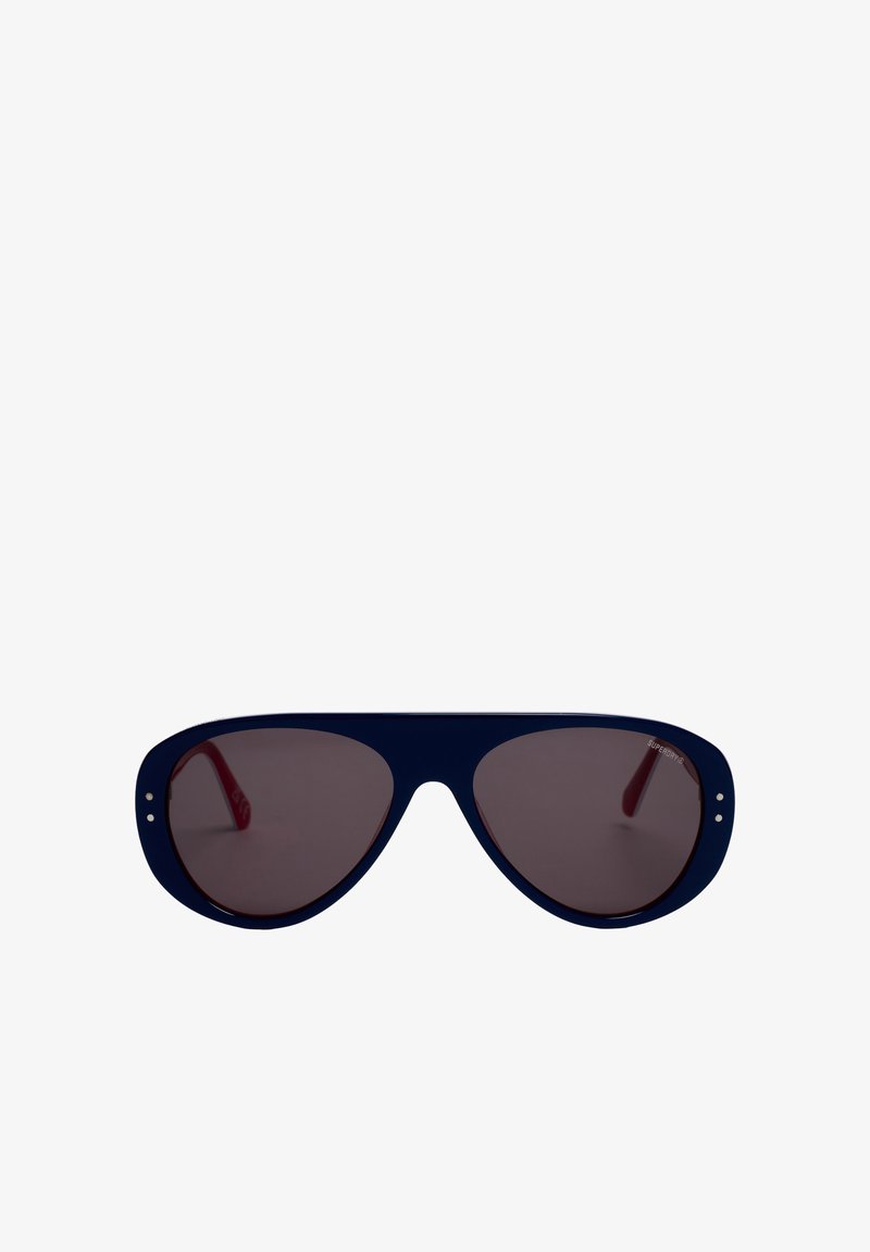 Lunettes de soleil aviateur oversize bleu foncé avec verres teintés et branches rouges, présentées sur fond blanc.