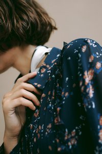 Navy blouse w kwiatowym wzorem z falbanami, z małymi pomarańczowymi i białymi kwiatkami, zakończony spiczastym kołnierzykiem i lekką teksturą.