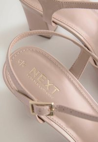 Paire d'escarpins à talons aiguilles rose nude à bride arrière avec boucle dorée et marquage « NEXT Forever Comfort » sur la semelle intérieure.
