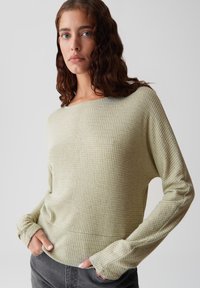 Pull en maille vert clair avec un col large et des manches longues, offrant une coupe décontractée et des détails côtelés aux poignets.