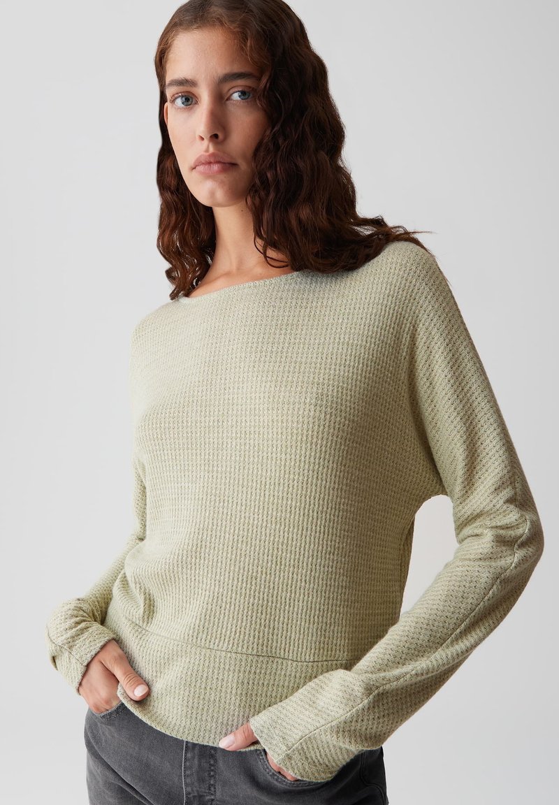 Pull en maille vert clair avec un col large et des manches longues, offrant une coupe décontractée et des détails côtelés aux poignets.