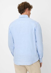 Camicia a maniche lunghe blu chiaro realizzata in tessuto testurizzato, con colletto standard e polsini con bottone, orlo arrotondato e dettagli sul giromanica posteriore.