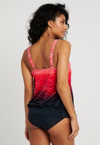 Haut de tankini avec un motif dégradé rose et rouge, bretelles ajustables et coupe ample, associé à un bas de maillot de bain bleu marine. Texture de tissu lisse.