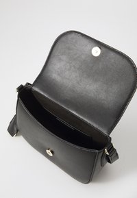 Borsa a spalla in pelle nera con pattina arrotondata, chiusura a scatto dorata e interno in suede. Include scomparti per carte e una tracolla regolabile.