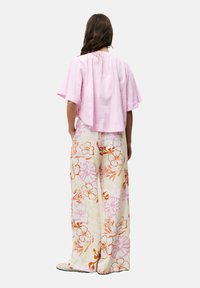 Roze cropped top met korte mouwen, gecombineerd met wijde bloemenbroek in witte, gele en oranje tinten.