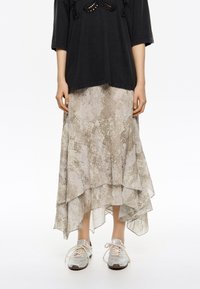 Falda midi fluida y con capas en beige claro con un sutil estampado de serpiente; combinada con una blusa negra holgada y zapatillas metálicas.