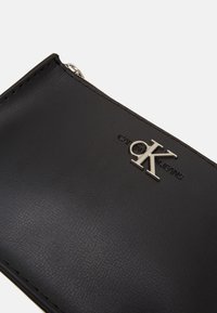 Portafoglio in pelle nera con logo CK in argento, chiusura zip e superficie testurizzata. Design compatto dallo stile minimalista.